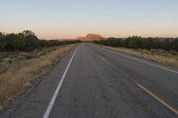 a long empty road with mountains in the distance with a car in the foreground