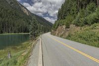 a large body of water next to a road with trees and mountains on it's sides