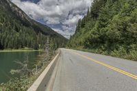 a large body of water next to a road with trees and mountains on it's sides