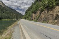 a large body of water next to a road with trees and mountains on it's sides