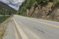 a large body of water next to a road with trees and mountains on it's sides