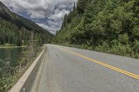 a large body of water next to a road with trees and mountains on it's sides