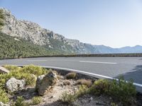 an asphalt roadway next to large rock formations on a mountain top with a curve in the middle