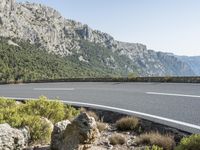 an asphalt roadway next to large rock formations on a mountain top with a curve in the middle