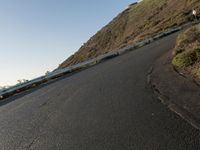 a black paved roadway is between hills and tall mastons on top of a hill