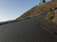 a black paved roadway is between hills and tall mastons on top of a hill