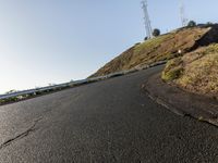 a black paved roadway is between hills and tall mastons on top of a hill