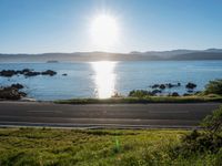 a scenic roadway leading to water next to the beach and hills in background during the sun