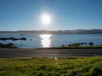 a scenic roadway leading to water next to the beach and hills in background during the sun