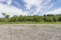 the large field is filled with stones and dirt with trees on the side and clouds in the sky