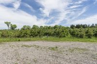 the large field is filled with stones and dirt with trees on the side and clouds in the sky