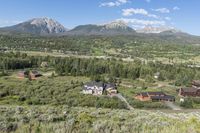 a rural setting with buildings, green trees and mountains in the background of blue skies