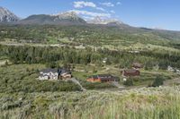 a rural setting with buildings, green trees and mountains in the background of blue skies