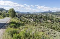 a rural setting with buildings, green trees and mountains in the background of blue skies