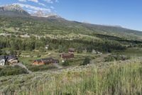 a rural setting with buildings, green trees and mountains in the background of blue skies