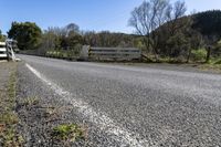 a white fence sitting next to an open road and tree filled fields under a blue sky