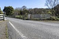 a white fence sitting next to an open road and tree filled fields under a blue sky