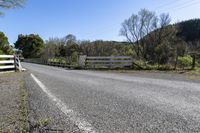 a white fence sitting next to an open road and tree filled fields under a blue sky