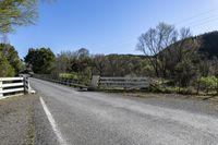 a white fence sitting next to an open road and tree filled fields under a blue sky