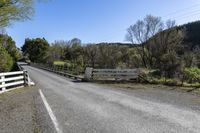 a white fence sitting next to an open road and tree filled fields under a blue sky