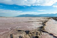 a lake of water with dirt, mud and sand below it and mountains in the background