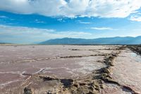 a lake of water with dirt, mud and sand below it and mountains in the background