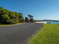 empty roadway by the beach with green grass and trees near by on hill at top