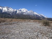 view of snowy mountains across a wide gravel path under a crescent sky with a blue sky