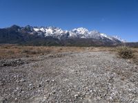 view of snowy mountains across a wide gravel path under a crescent sky with a blue sky