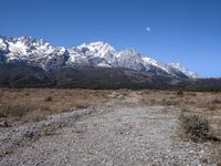 view of snowy mountains across a wide gravel path under a crescent sky with a blue sky