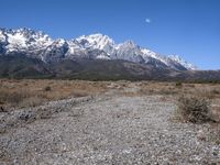 view of snowy mountains across a wide gravel path under a crescent sky with a blue sky