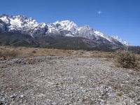 view of snowy mountains across a wide gravel path under a crescent sky with a blue sky