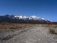 view of snowy mountains across a wide gravel path under a crescent sky with a blue sky