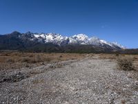 view of snowy mountains across a wide gravel path under a crescent sky with a blue sky