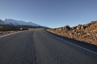 the deserted road is very wide and paved and has rocky hills in it under blue skies