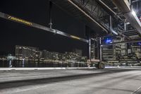 an empty city street next to the water at night time with a light show on a bridge