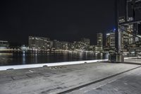 an empty city street next to the water at night time with a light show on a bridge