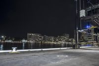 an empty city street next to the water at night time with a light show on a bridge