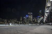 an empty city street next to the water at night time with a light show on a bridge