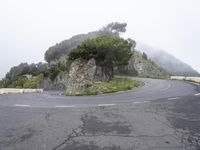 an empty winding road on the side of the mountain covered in clouds and mists