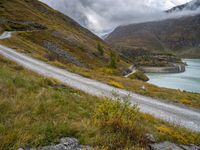 a view looking down at a winding trail with a lake in the background on a cloudy day