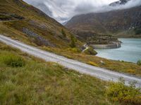 a view looking down at a winding trail with a lake in the background on a cloudy day