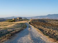 dirt road, dirt field and mountain range with blue sky, tuscany hills, sun, cloudless sky and small building