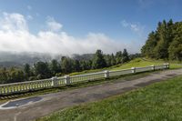 a paved walkway on a hillside next to a forest and foggy hill tops of the surrounding mountains