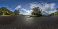 a curved street has some trees and hills in the background and clouds in the sky