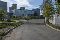 a city street surrounded by grass and tall buildings at the end of a street there is a paved pathway in front of the building