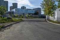 a city street surrounded by grass and tall buildings at the end of a street there is a paved pathway in front of the building