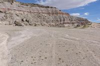 a lone yellow and gray van parked on the side of a rocky road in front of a large rock formation