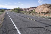 a bicycle rider is stopped on a long empty road in the desert near mountains and mountains