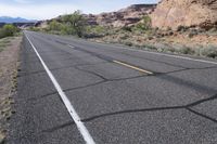 a bicycle rider is stopped on a long empty road in the desert near mountains and mountains